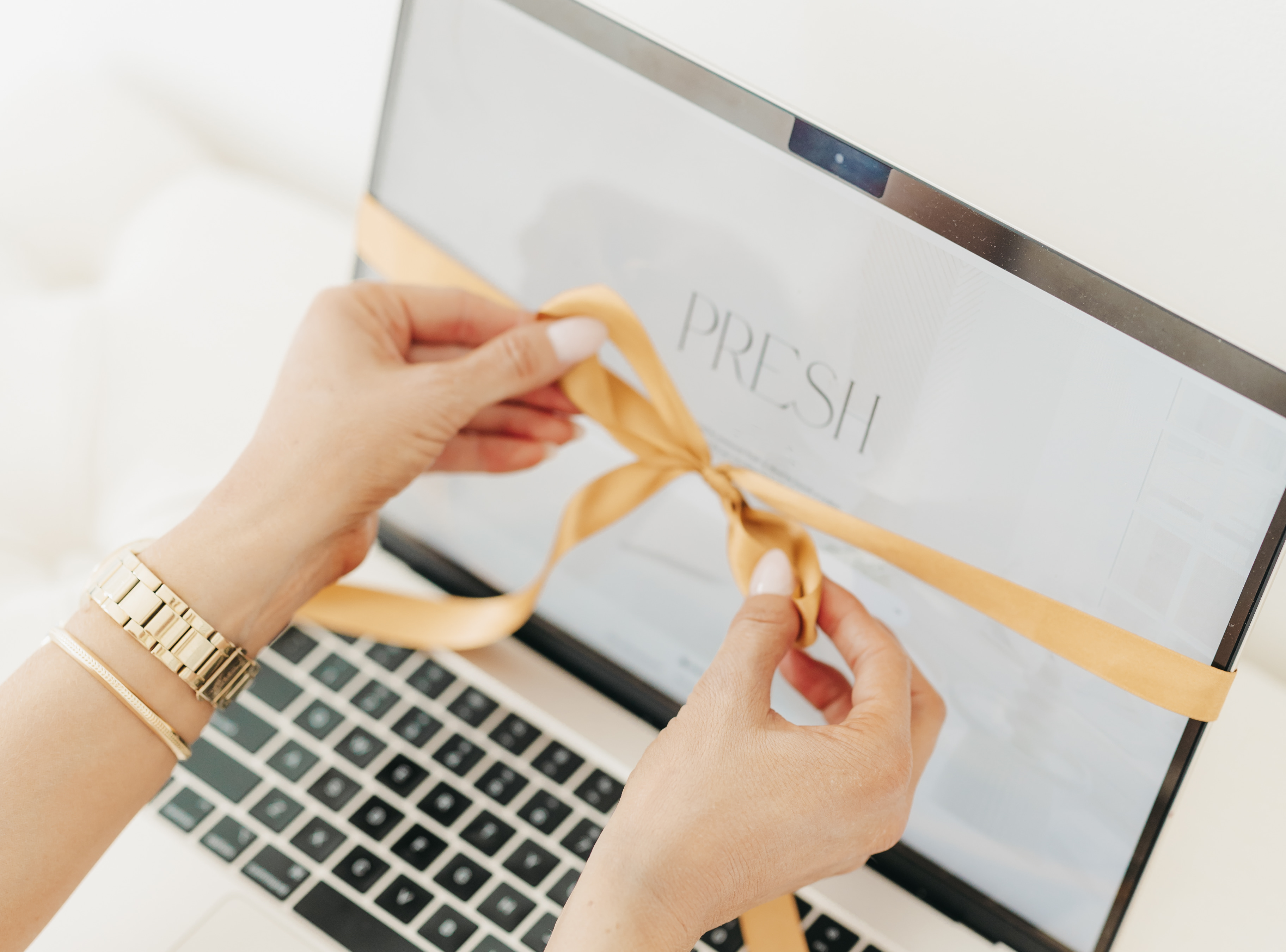 Person tying a yellow ribbon around a laptop on a white surface